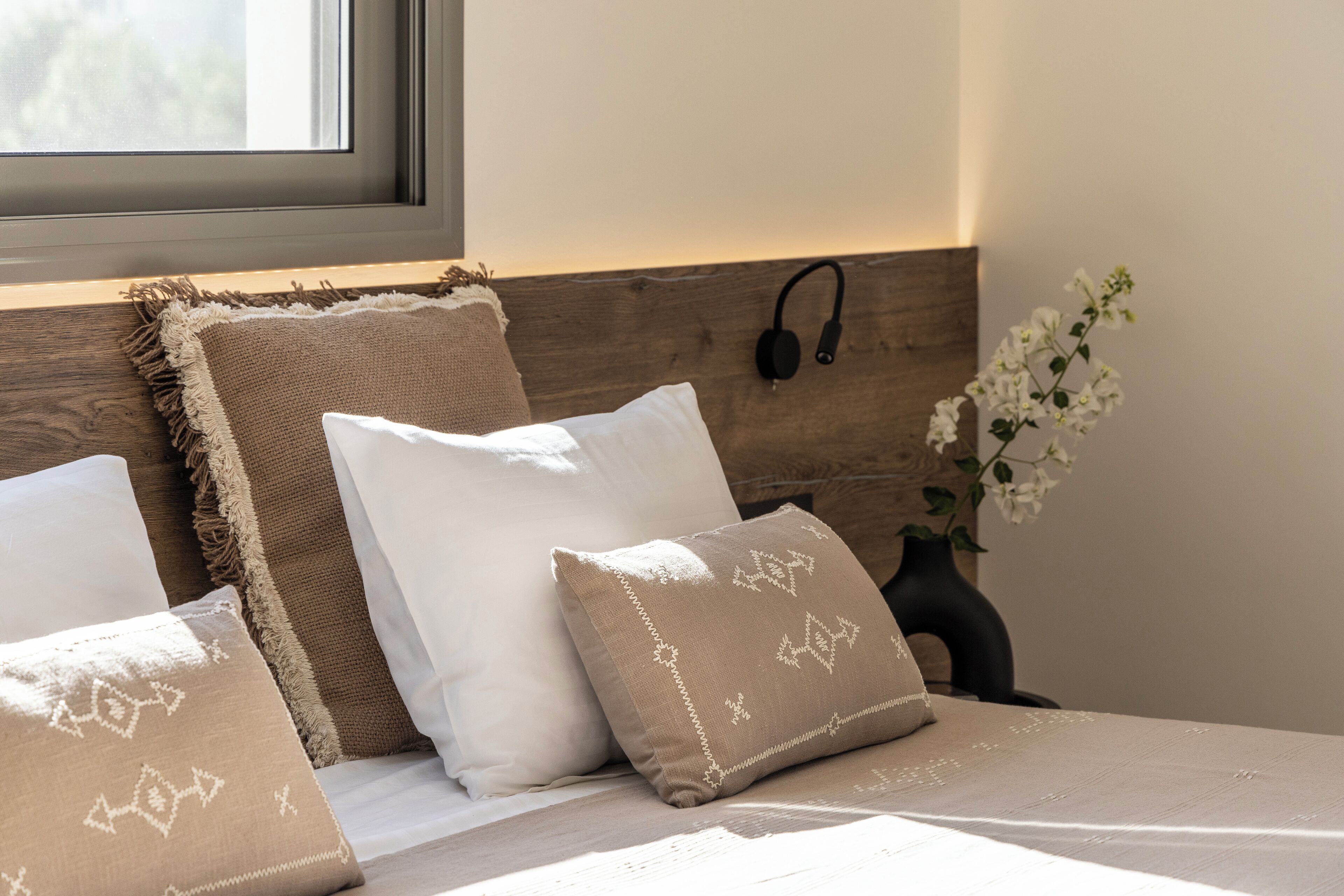 Una cama bien hecha con cabecera, almohadas y una mesita de noche con un jarrón de flores.
