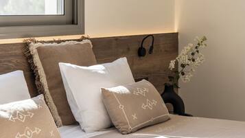 Una cama bien hecha con cabecera, almohadas y una mesita de noche con un jarrón de flores.
