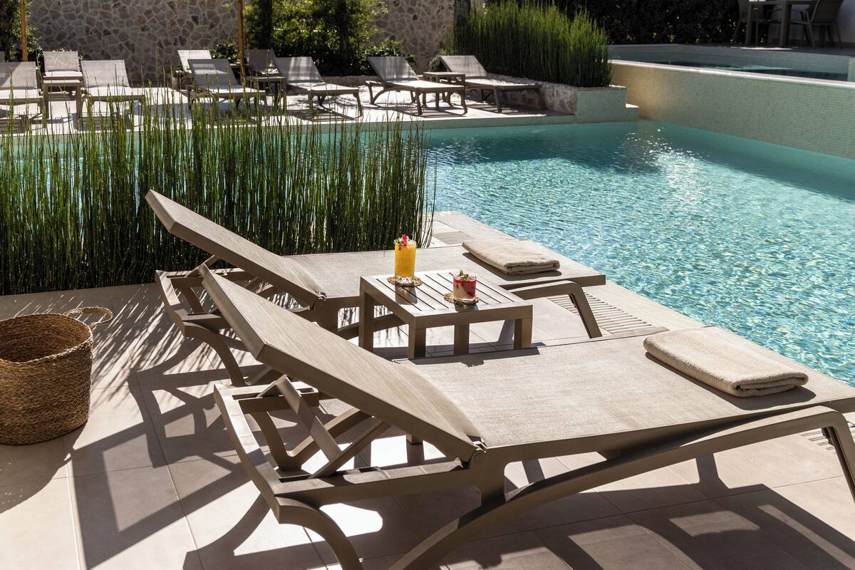 Zona de piscina con sillones, una mesa, una bebida y una cesta.