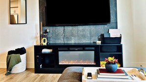 Una sala de estar moderna con un televisor de pantalla plana montado en una pared de piedra, una chimenea con frente de vidrio y una zona de estar acogedora con un sofá y una mesa de centro.
