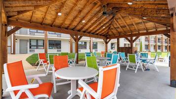 An outdoor covered patio with wooden beams, colorful chairs, and tables.