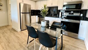 Una cocina moderna con electrodomésticos de acero inoxidable, armarios blancos y una mesa de comedor de vidrio con dos sillas.