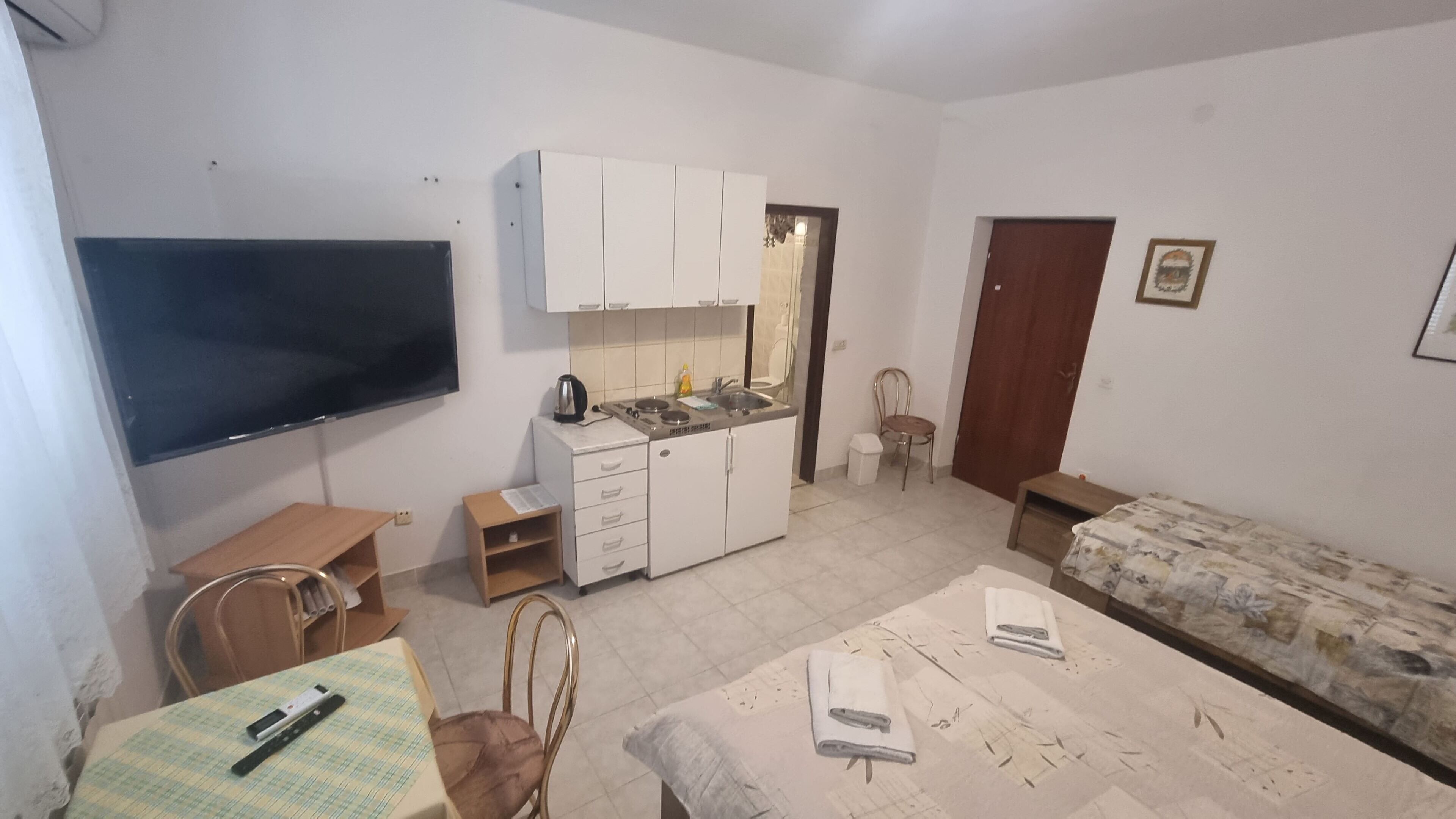 A compact living space with a kitchenette, a flat-screen TV, a sofa, and a dining area.