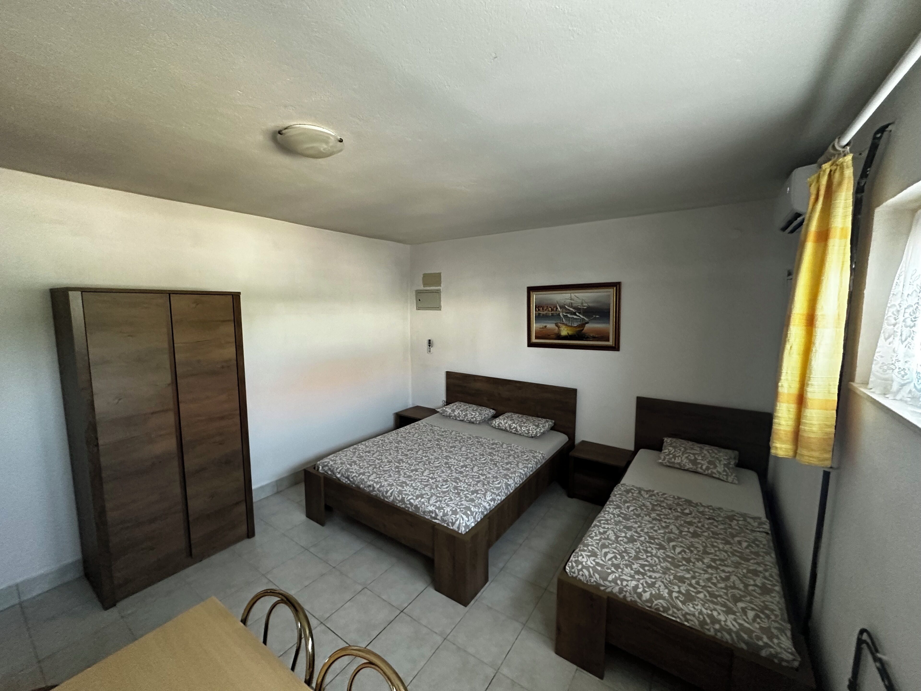 A bedroom with two beds, a wardrobe, a small table, and a painting on the wall.