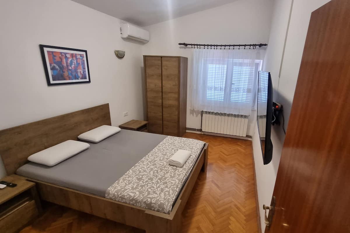 A bedroom with a wooden bed, a nightstand, a wardrobe, and a window with white curtains.