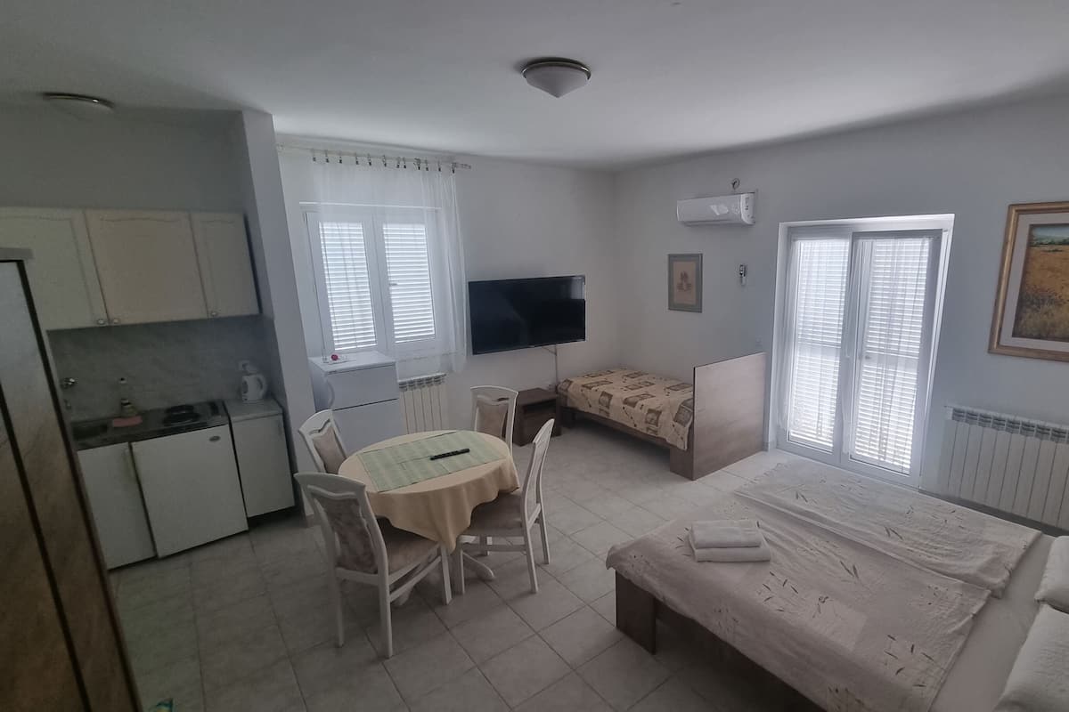 A compact room with a kitchenette, a bed, a small table with chairs, and a TV.