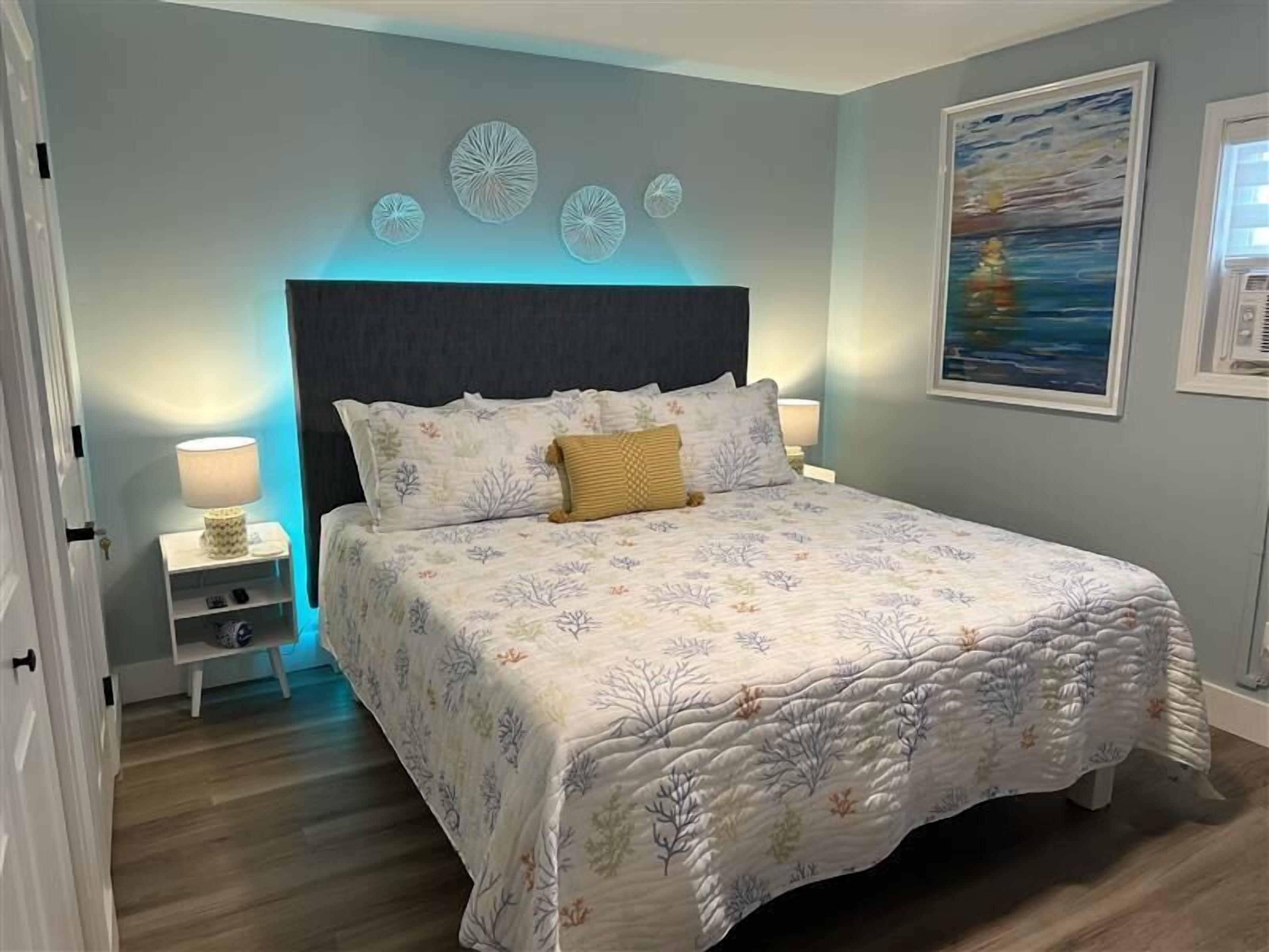 A bedroom with a bed, nightstands, a wall clock, and a painting.