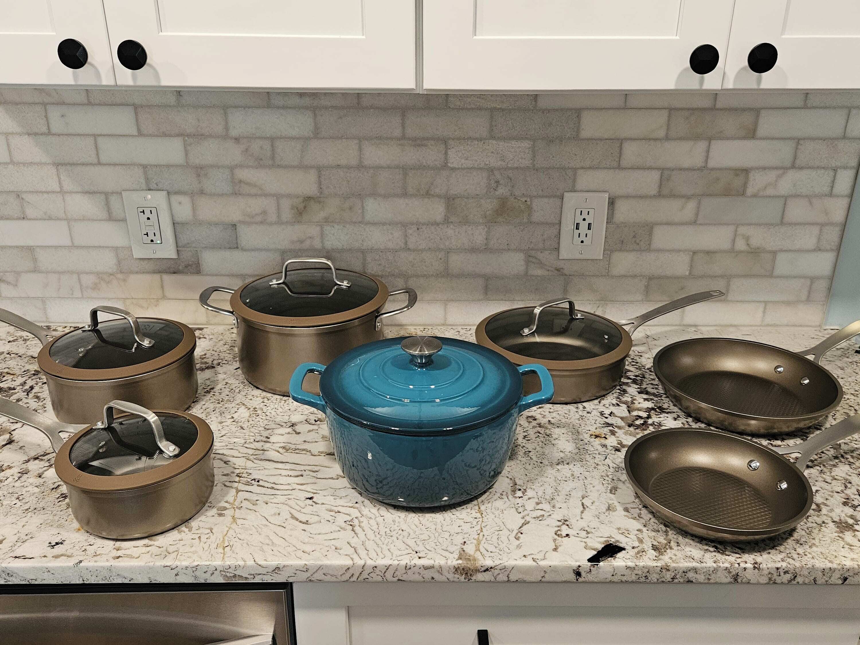 A kitchen with white cabinets, a marble countertop, and various cookware including pots and pans.