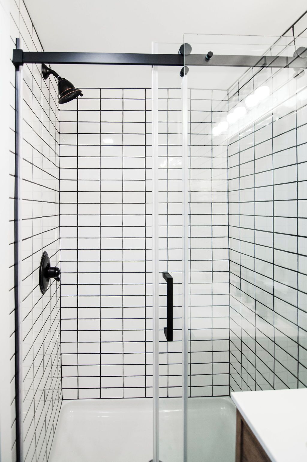 A modern bathroom with white subway tiles, a glass shower enclosure, and a black faucet.