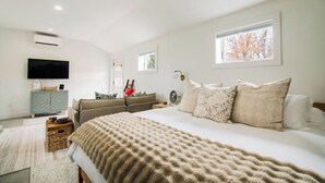 Een slaapkamer met een groot bed, een aan de muur bevestigde televisie, een dressoir en een raam met uitzicht op bomen.