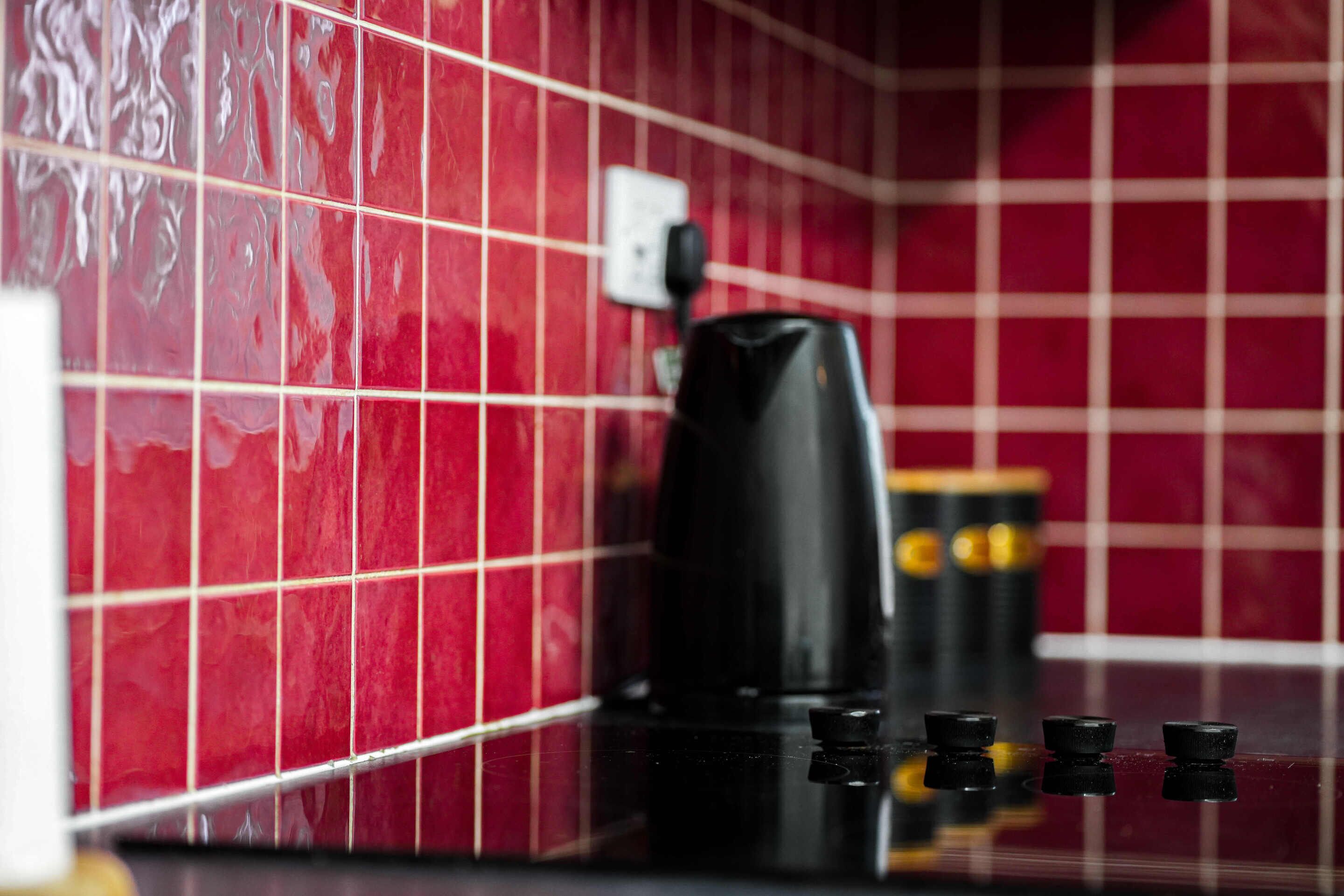 Une cuisine aux murs recouverts de carreaux rouges et un appareil à café posé sur le plan de travail.
