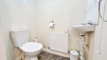 A small, white bathroom with a toilet, a radiator, a sink, and a trash bin.