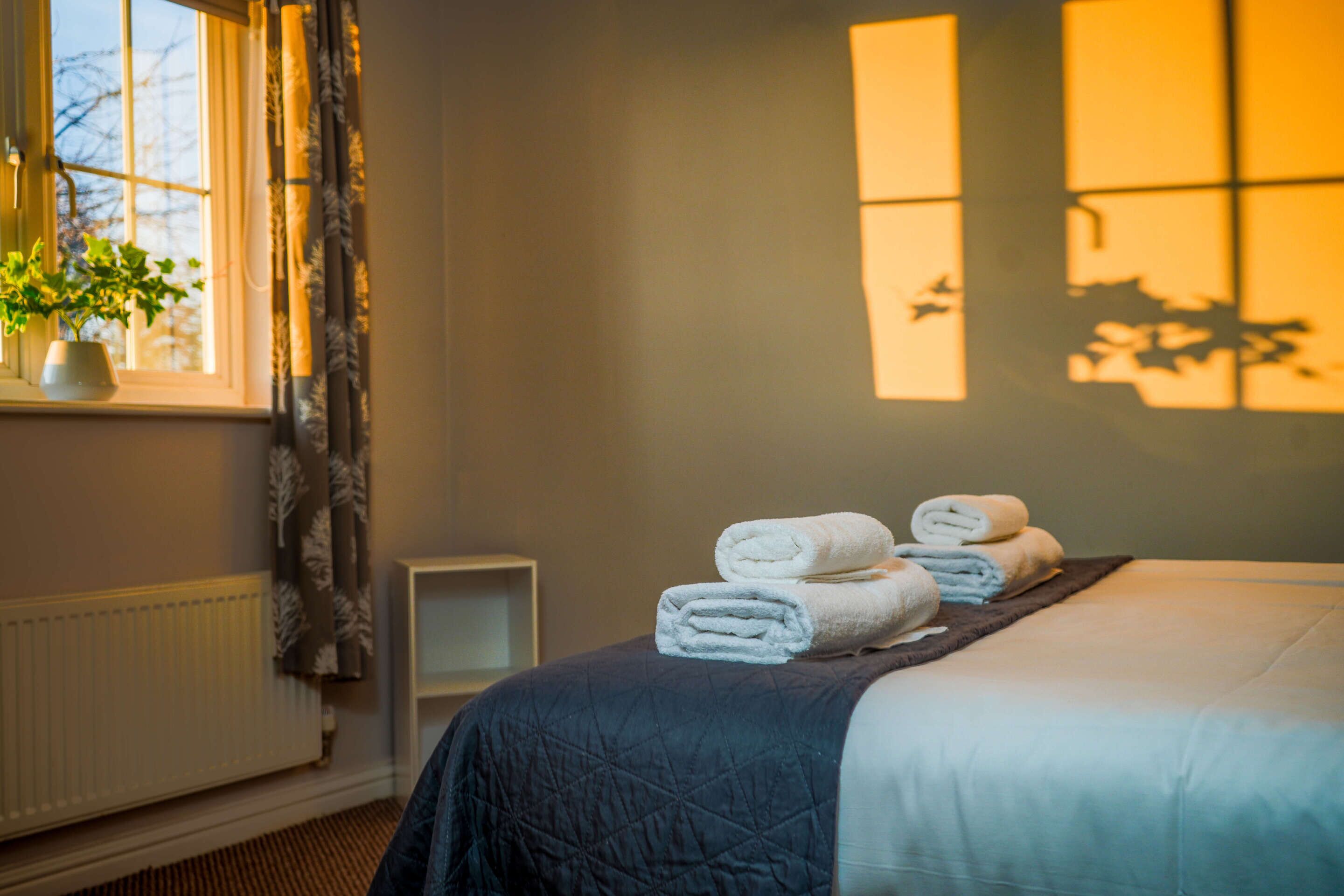 Habitación de hotel con cama, ventana con cortinas, radiador y una planta en el alféizar.