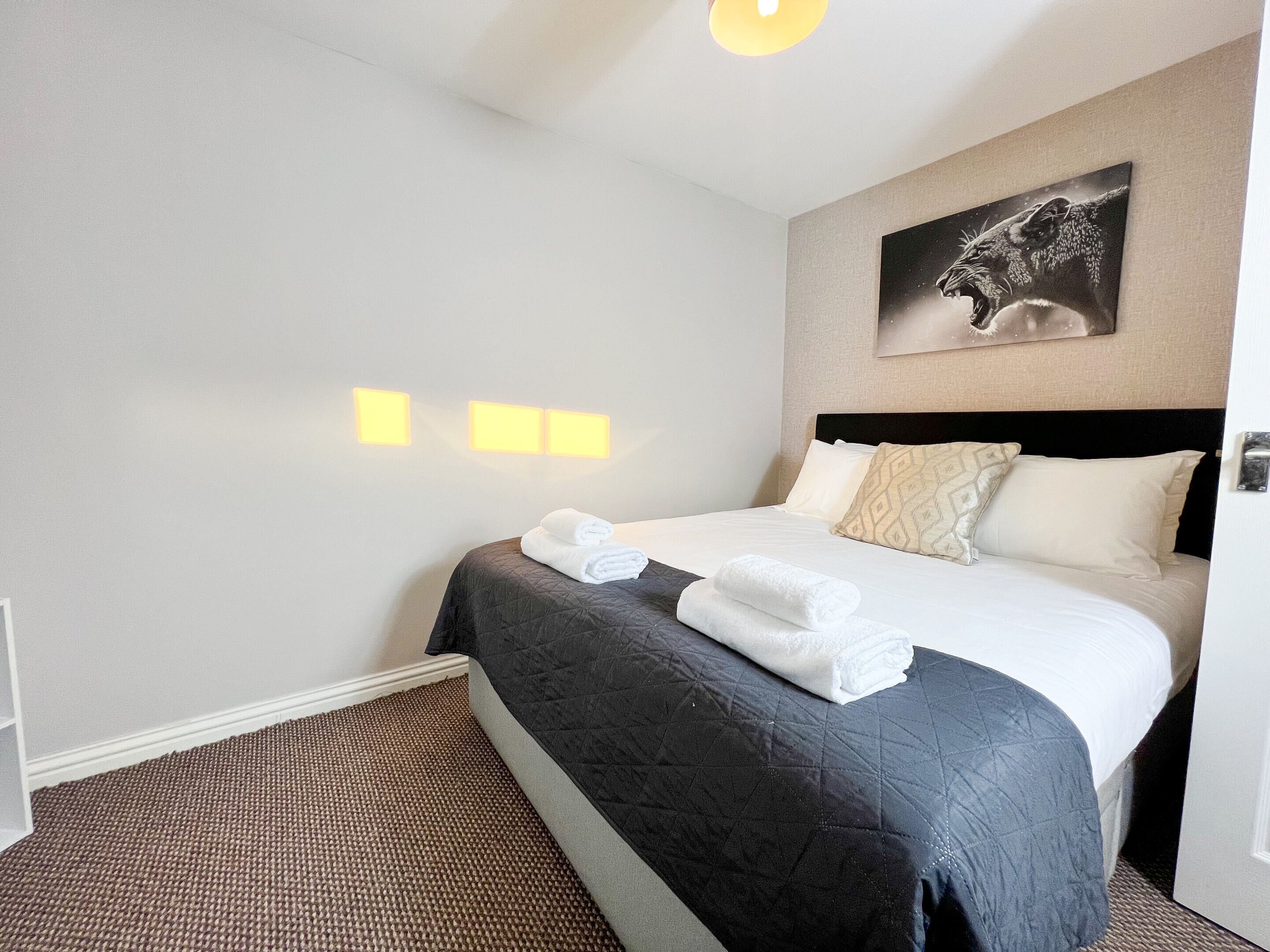 Ein Hotelzimmer mit Bett, Kopfteil, Wandbild und zwei Wandleuchten.