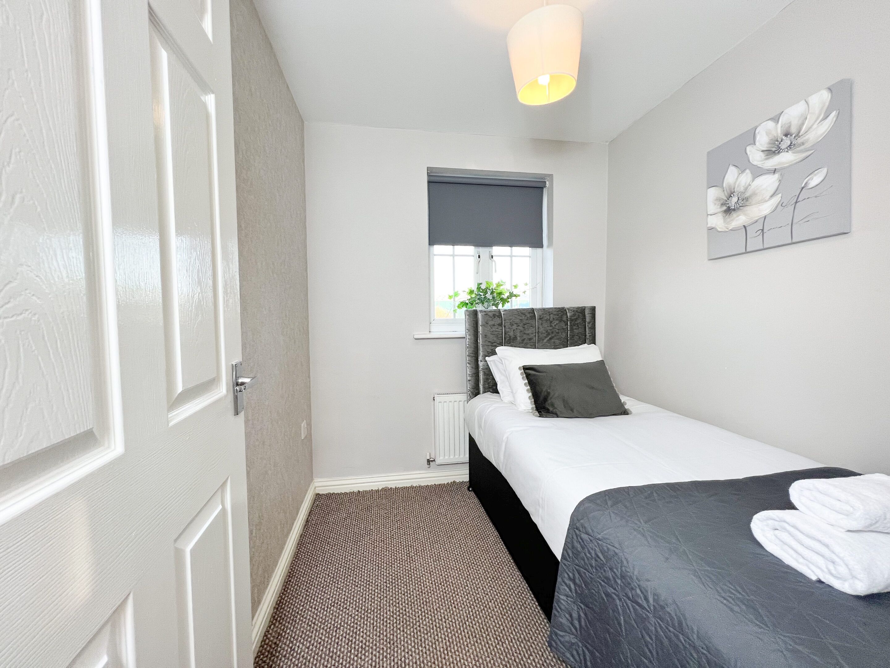 A bedroom with a bed, a radiator, a window with a plant, and a wall with a floral painting.