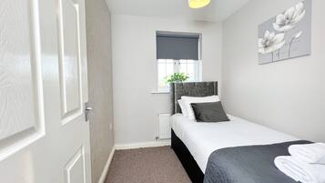 A bedroom with a bed, a radiator, a window with a plant, and a wall with a floral painting.