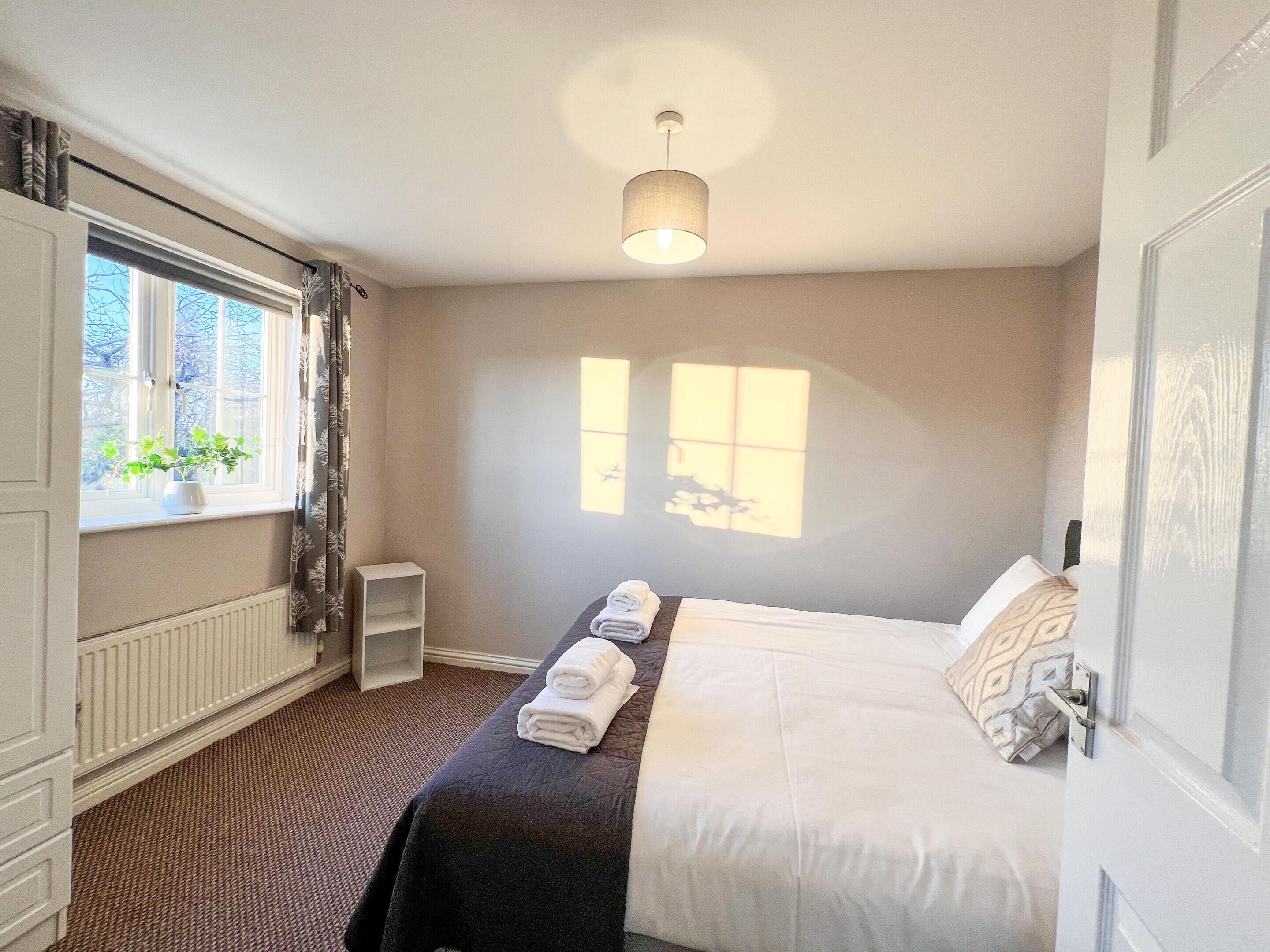 A hotel room with a bed, a window, a radiator, and a ceiling light.