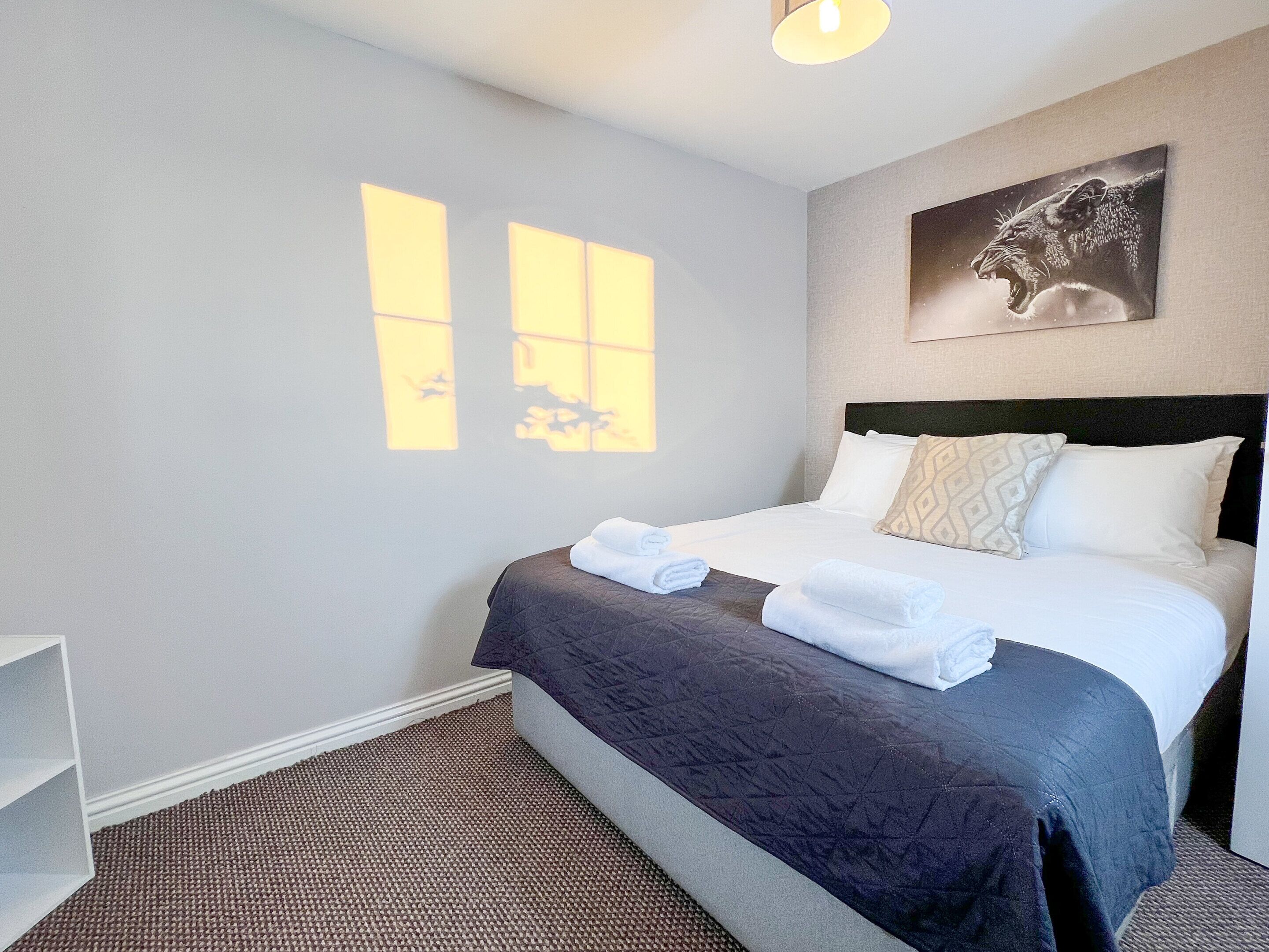 A hotel room with a bed, a headboard, a wall-mounted artwork, and a window with a view of the sky.
