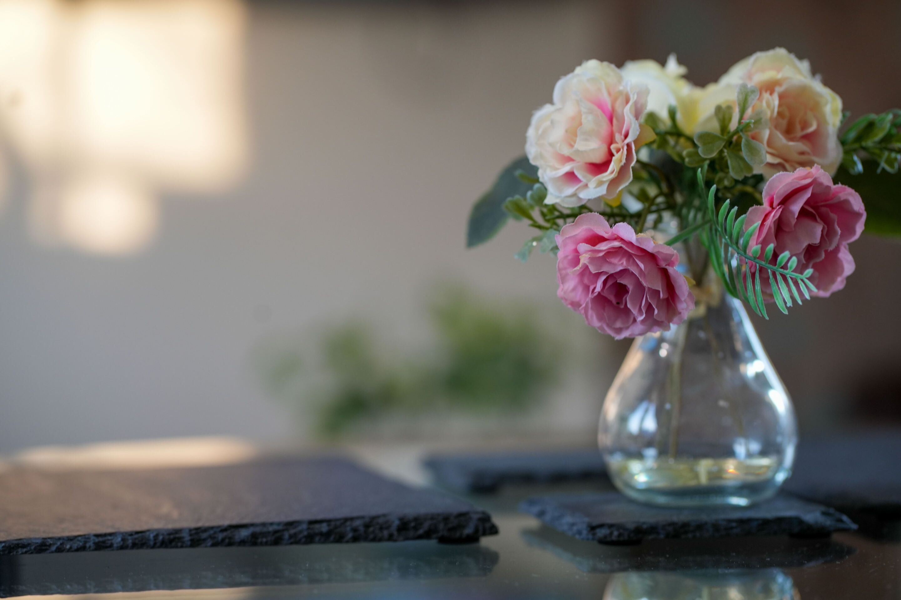 Un vase en verre transparent contenant des fleurs roses et blanches, posé sur une surface réfléchissante.