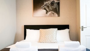 Una cama bien hecha con un edredón oscuro, dos almohadas y dos toallas dobladas.