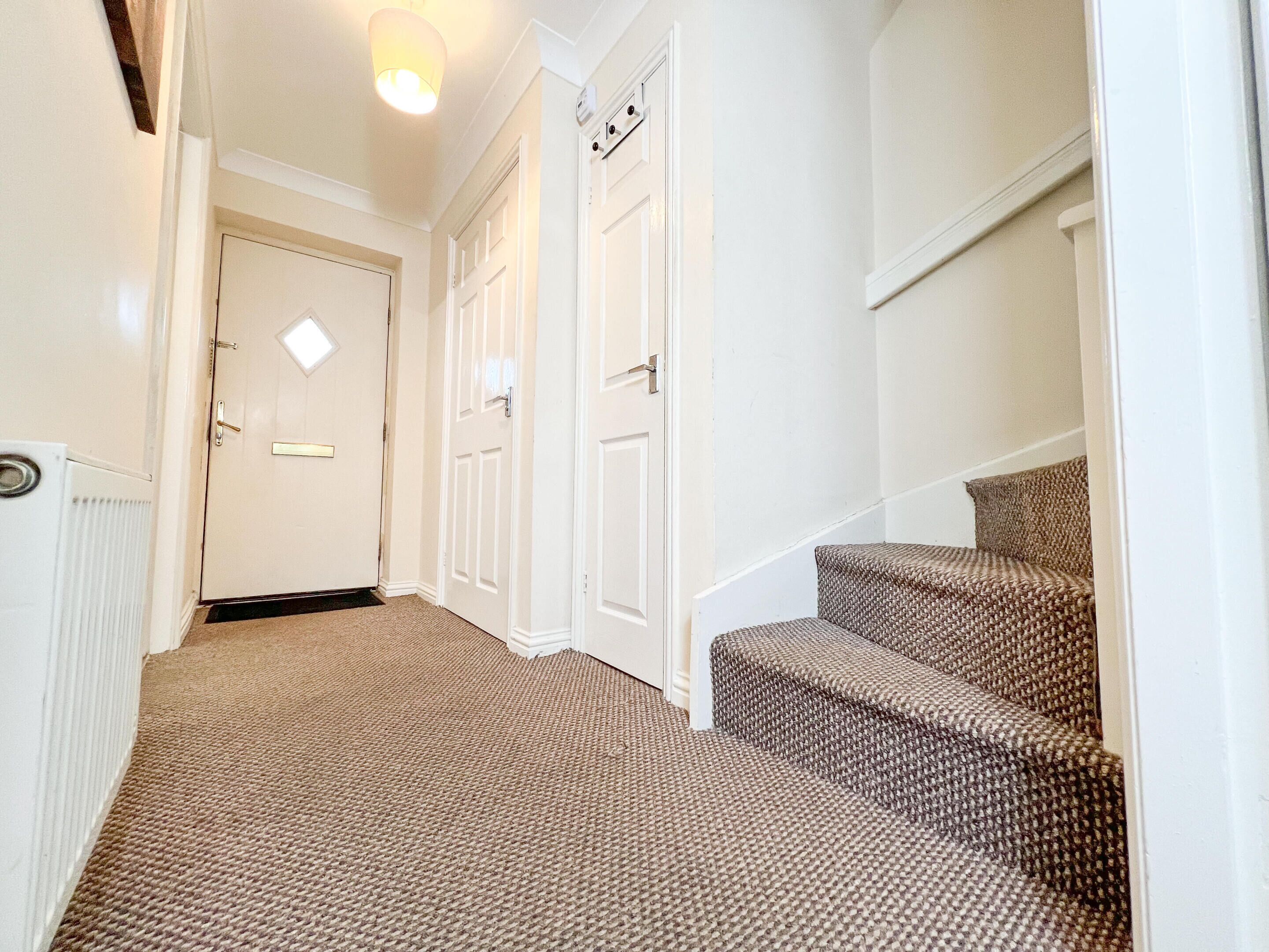 Un couloir recouvert de moquette, avec des portes blanches et un escalier dont les marches sont recouvertes d’une moquette à motifs.