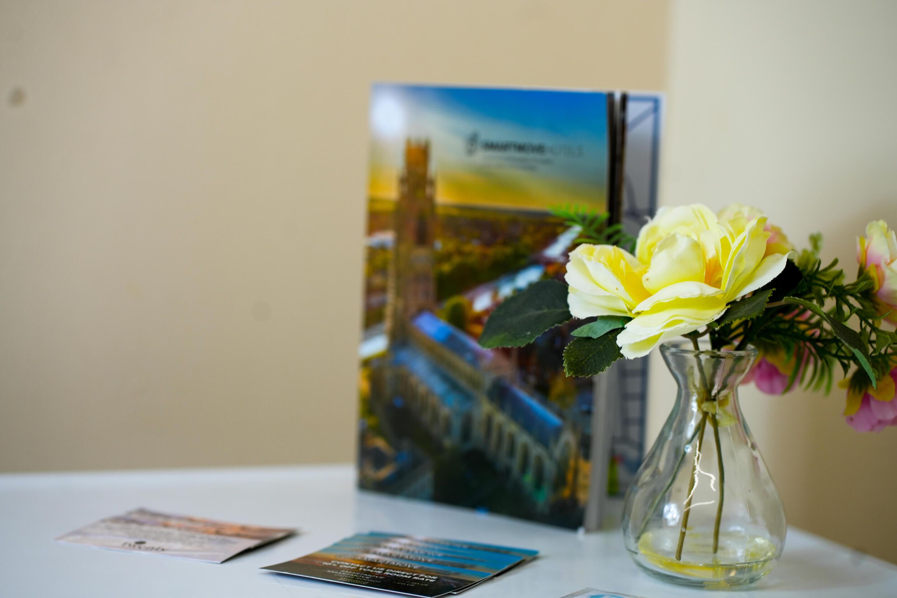 Une table avec un vase de fleurs et une brochure.
