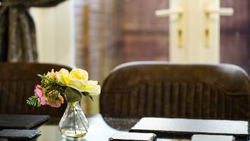 A table with a vase of flowers, a menu, and a window with a view of a building.