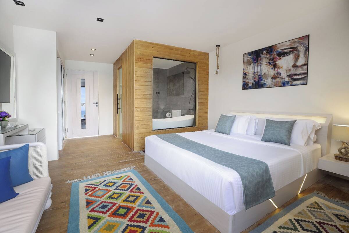 A modern hotel room with a large bed, a bathroom with a bathtub, and a view of the hallway.