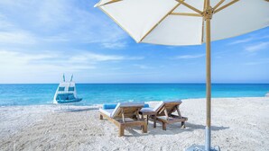 Een strand met een witte parasol, twee houten ligstoelen en een blauwe strandstoel.