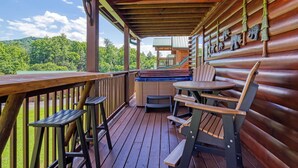 Um deck de madeira com área de estar externa, banheira de hidromassagem e vista para uma área arborizada.