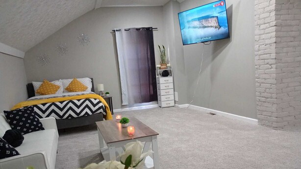 A modern bedroom with a bed, a TV mounted on the wall, and a small table with a candle.