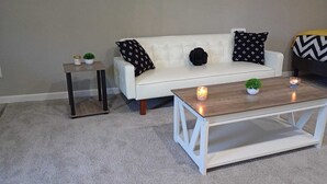 A living room with a white sofa, two black pillows, a small side table, a coffee table, and two lit candles.