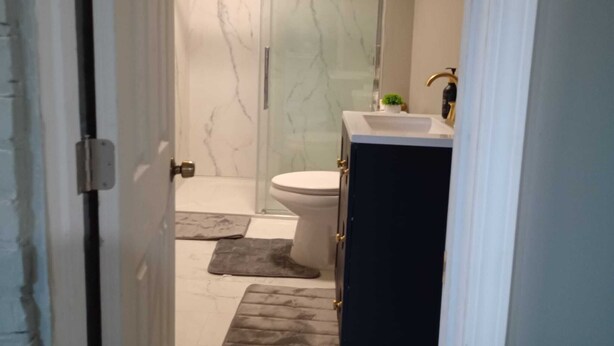 A bathroom with a glass shower enclosure, a toilet, and a sink with a small plant on the counter. - Up Unit Studio in West CLE (Cleveland)