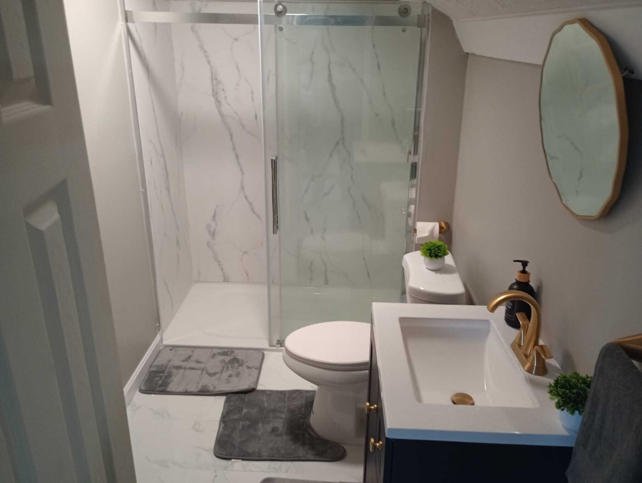 Et badeværelse med en brusekabine i glas, et toilet, en vask med guldfarmet hane og et spejl på væggen.