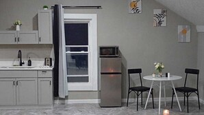 A compact kitchen with a refrigerator, microwave, and sink. There is a dining area with two chairs and a small table. The room has a sloped ceiling and a window. - Up Unit Studio in West CLE (Cleveland)