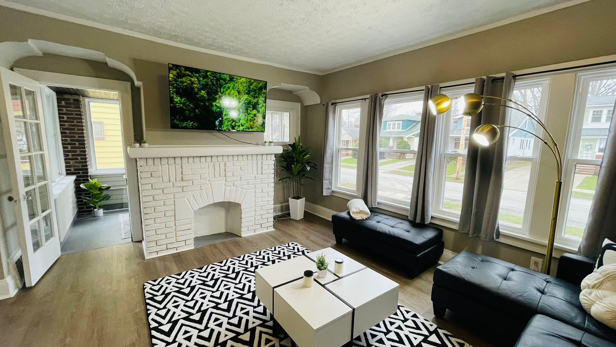 A living room with a fireplace, a black leather sofa, a coffee table, and a large TV screen.