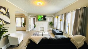 A living room with a fireplace, a sofa, a TV, and a large window with curtains. - City Slicker Suite West CLE (Cleveland)