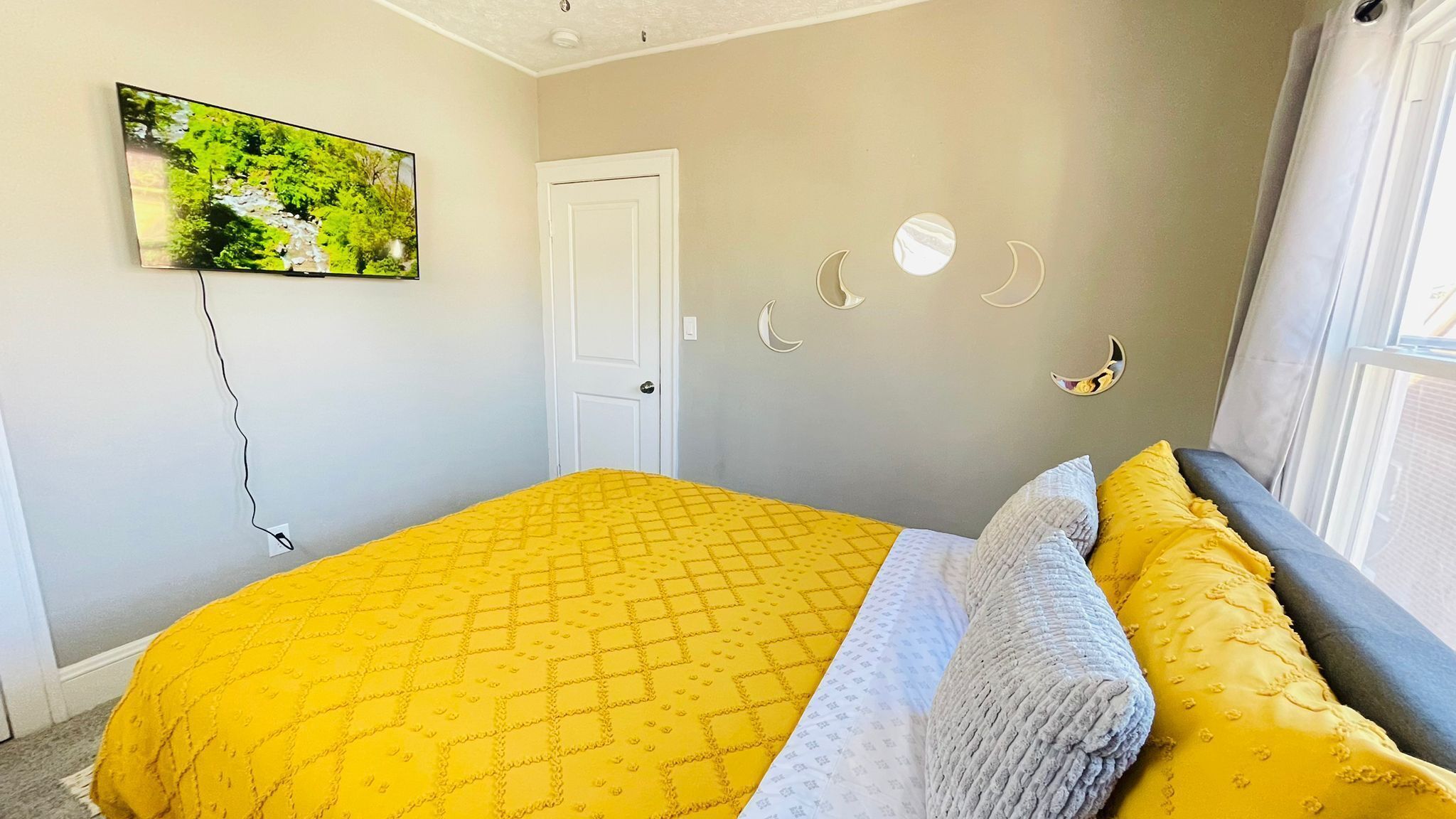 A bedroom with a bed, a door, a wall-mounted picture, and a window.