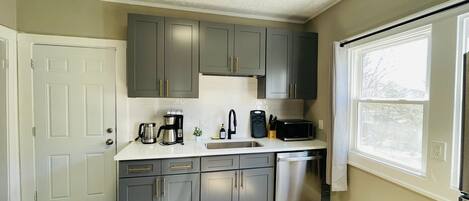 A modern kitchen with grey cabinets, a white countertop, a stainless steel dishwasher, and a window providing natural light.