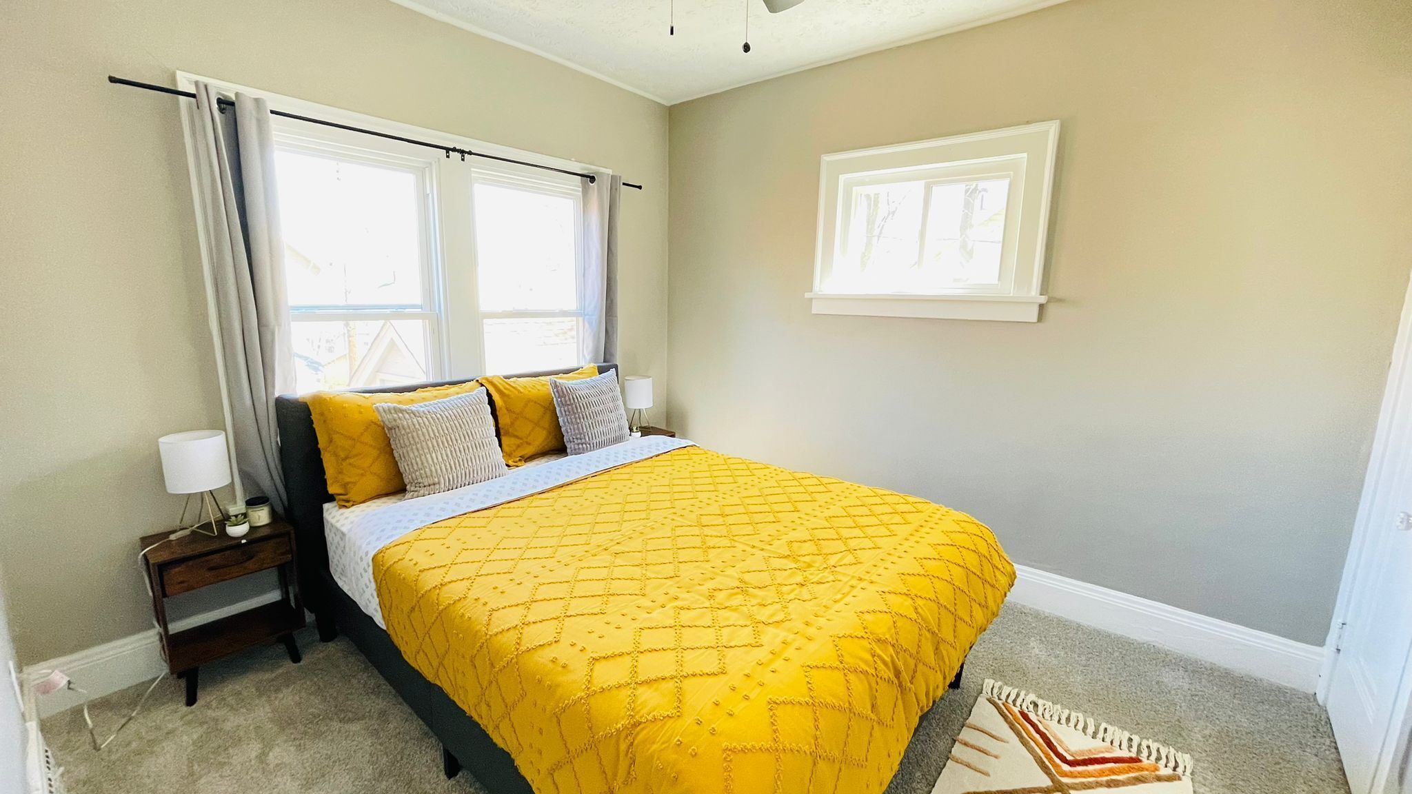 Une chambre à coucher avec un lit, une table de chevet, une lampe, une fenêtre avec des rideaux et un tapis.