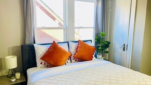A neatly made bed with patterned bedding, a bedside lamp, and a small plant on the nightstand. - The Stargazer Sunroom 2bedroom in West CLE (Cleveland)