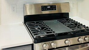 A kitchen with a stainless steel stove, a black range hood, and grey cabinets with gold handles. - The Stargazer Sunroom 2bedroom in West CLE (Cleveland)