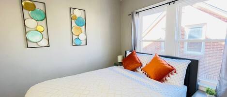 A bedroom with a bed, pillows, a nightstand, a window, and wall art.