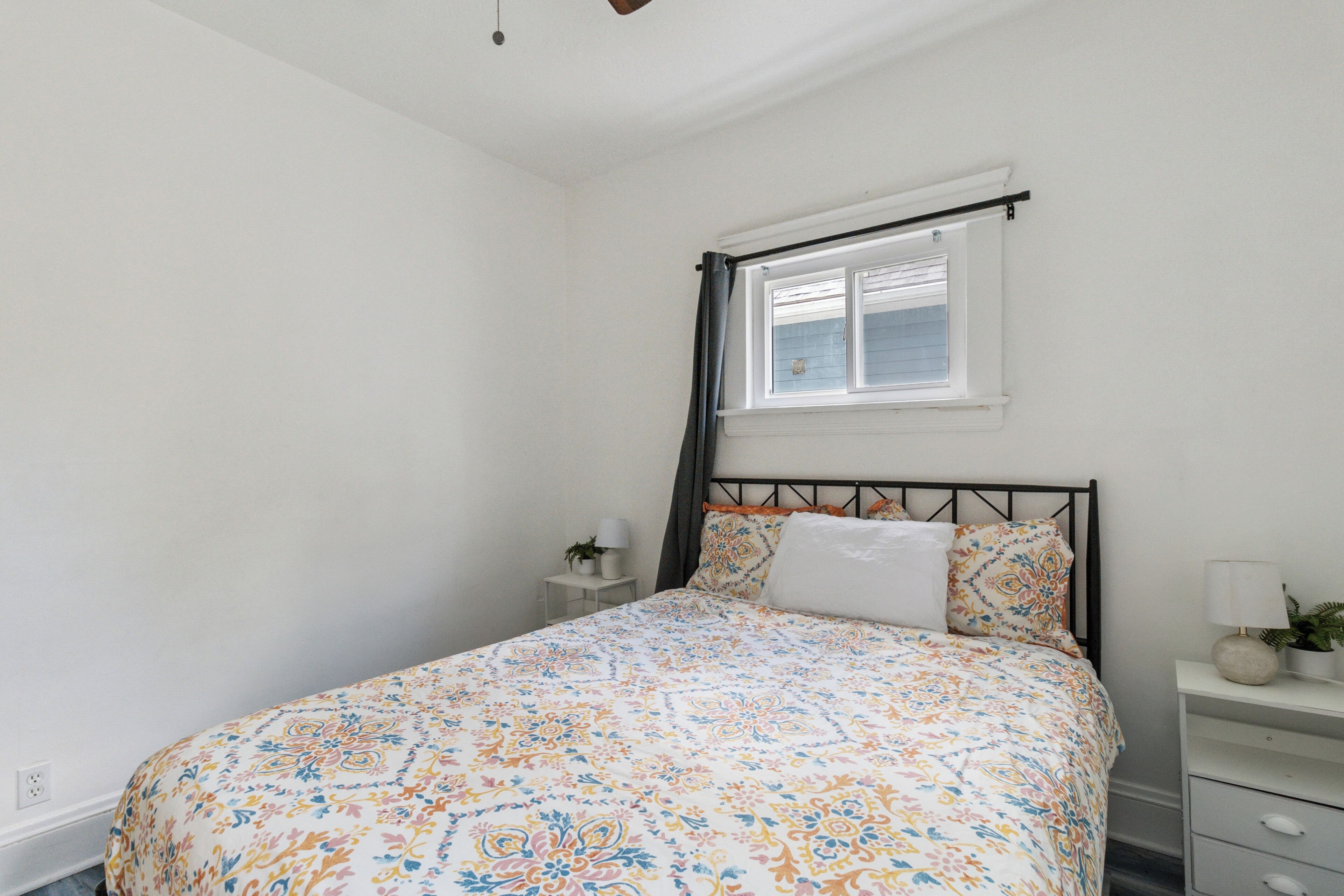 A bedroom with a bed, a window, a nightstand, and a lamp.