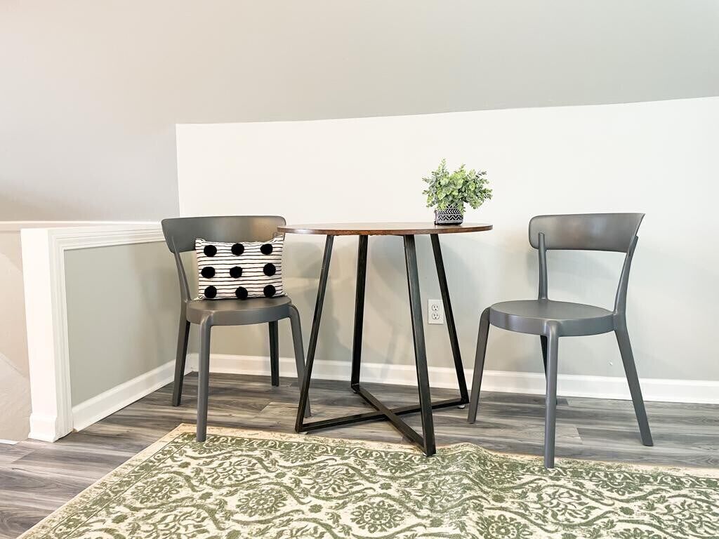 Un coin salon avec deux fauteuils et une petite table, une plante en pot et un tapis à motifs.
