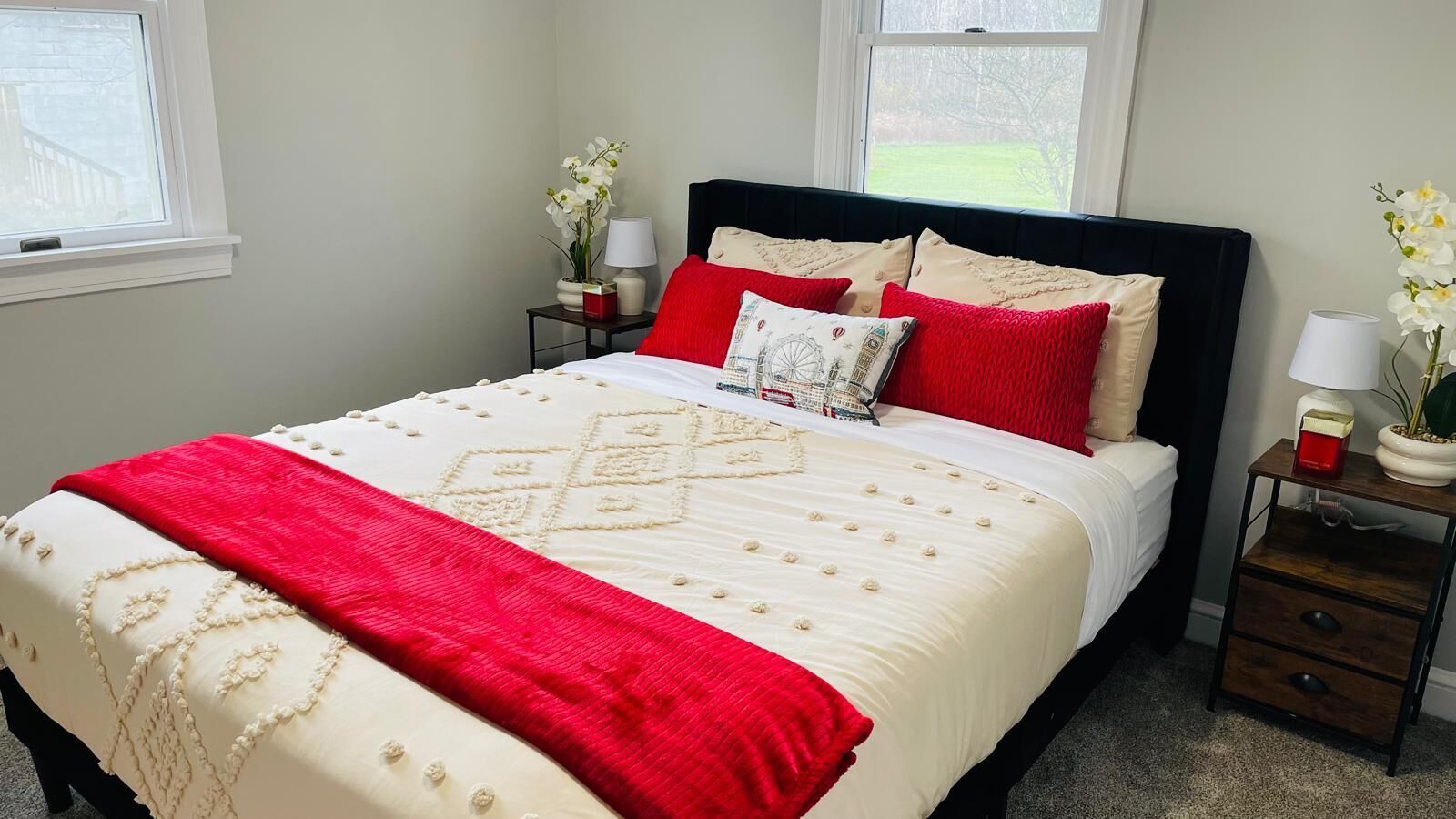 A neatly made bed with a red and white bedspread, two nightstands with lamps, and a window with a view of greenery.
