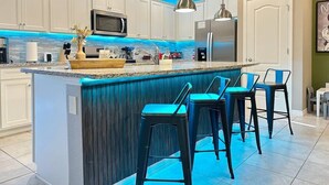 A modern kitchen with white cabinets, a central island with bar stools, and blue lighting accents. - This townhouse is a 5 bedroom(s), 4.5 bathrooms, located in Davenport, FL. (Davenport)