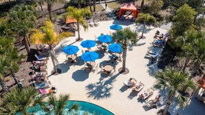 An aerial view of a resort with a pool, sun loungers, umbrellas, and palm trees. - This townhouse is a 5 bedroom(s), 4.5 bathrooms, located in Davenport, FL. (Davenport)