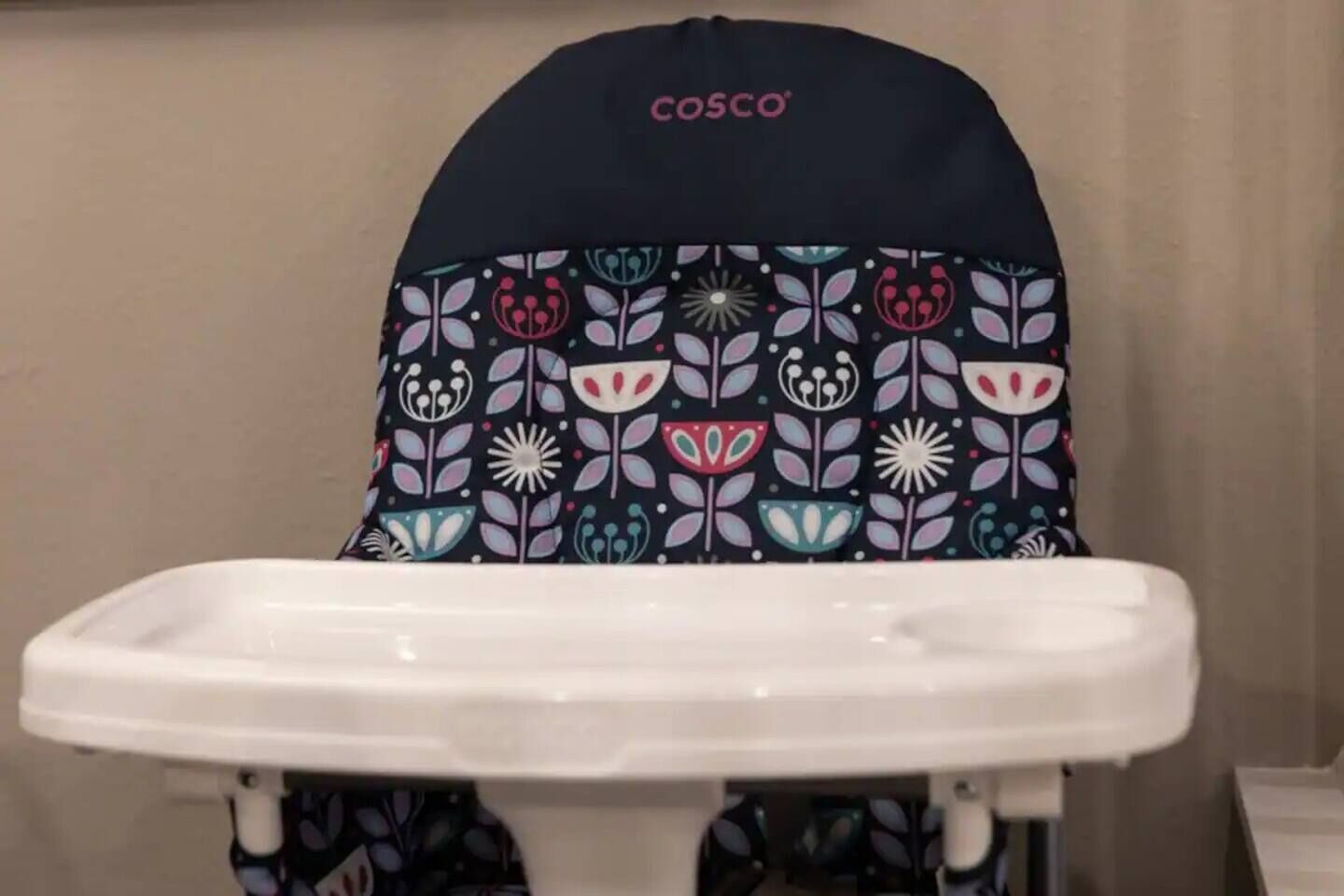 Una trona para bebé con funda estampada de colores y una bandeja blanca.