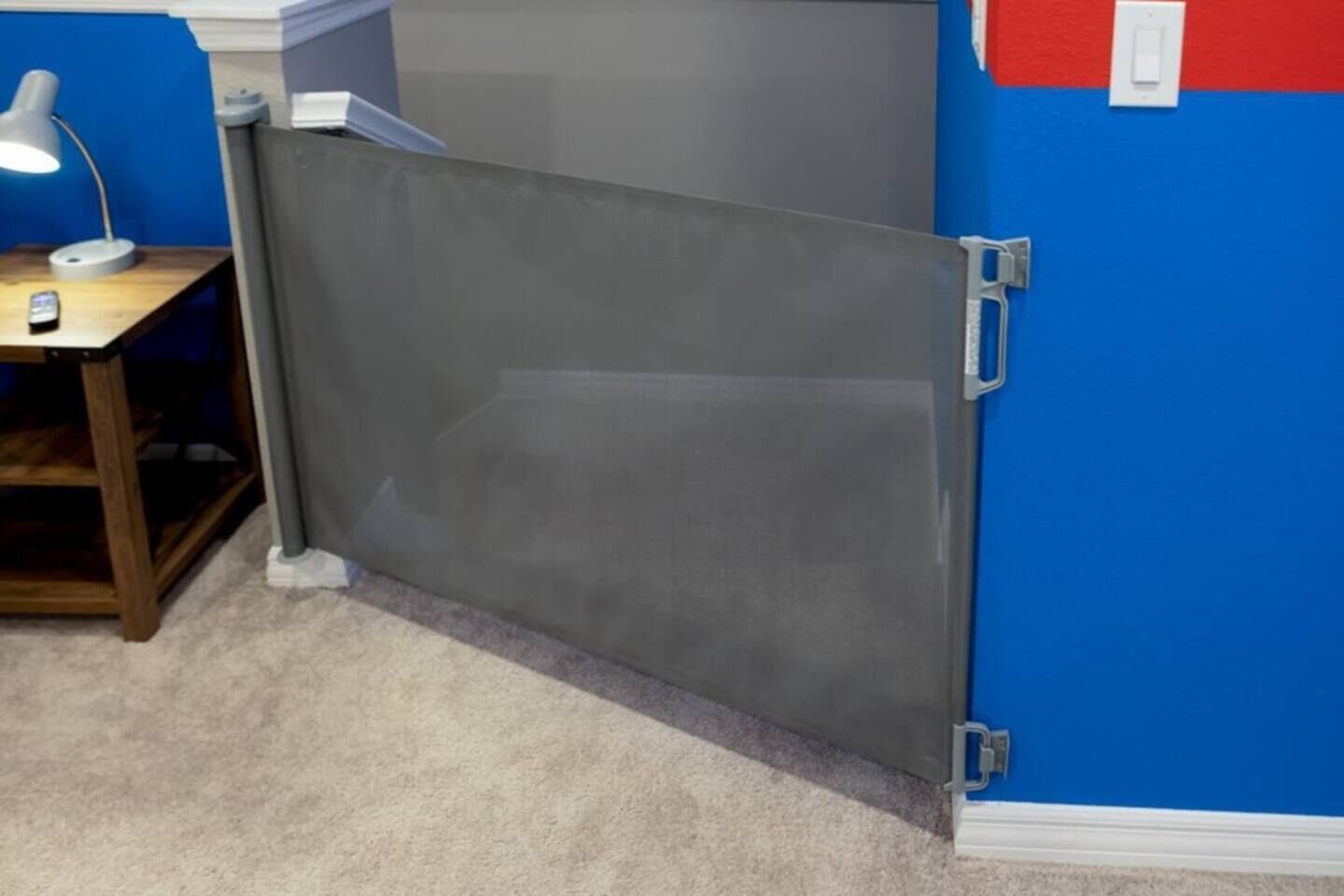 A room with a grey partition, a desk with a lamp, and a blue wall with a red section.